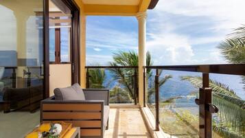 A balcony with a sofa and a table, overlooking a scenic view with palm trees and a clear sky.