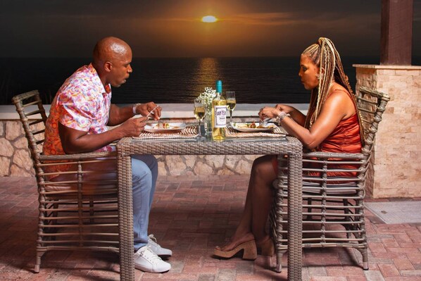 Two people dining at an outdoor table with a view of the ocean.