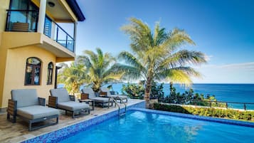 A poolside area with lounge chairs and a view of the ocean.