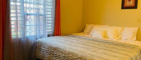 A room with a bed, a window with curtains, and a framed picture on the wall.