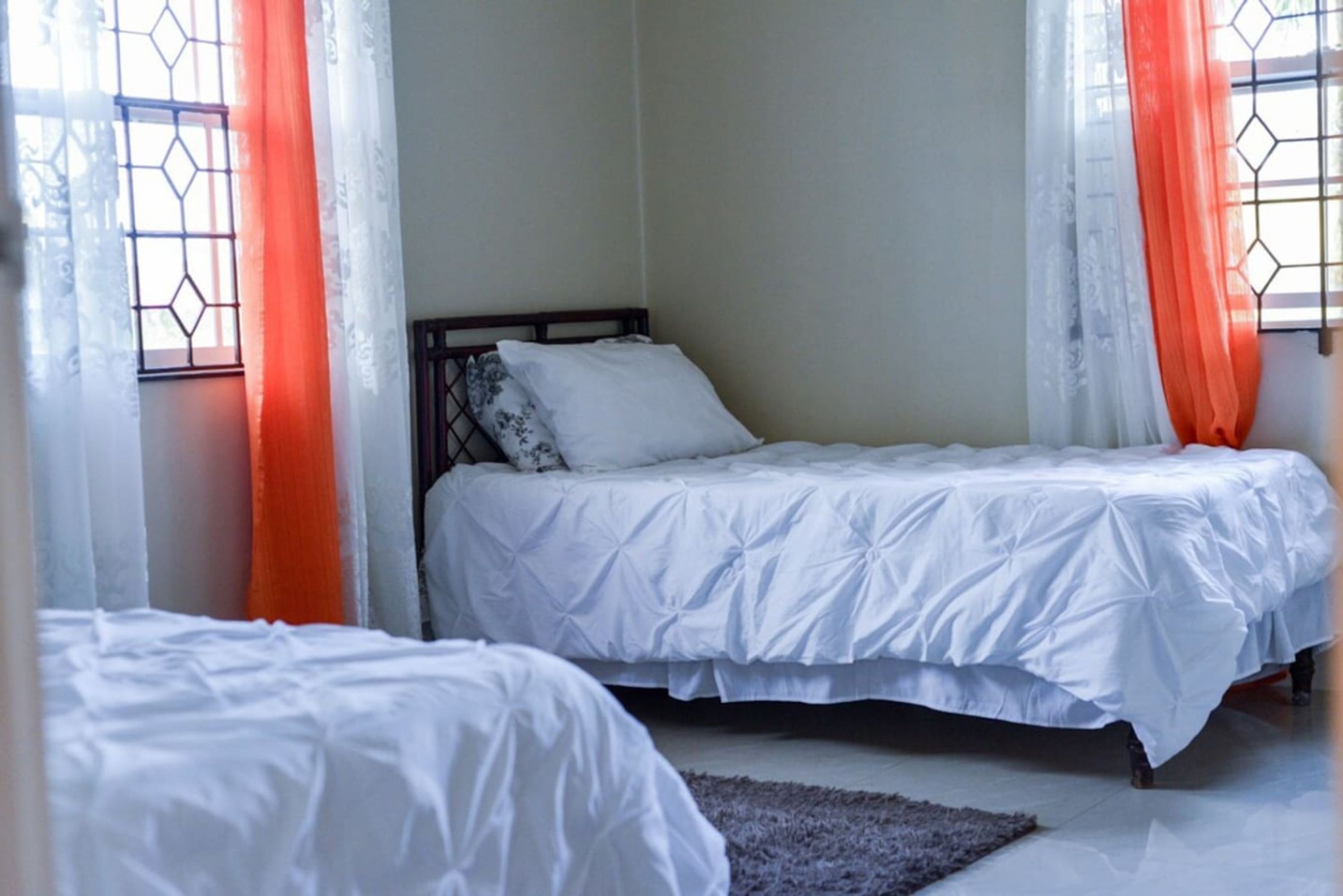 A bedroom with two single beds, a window with a metal grille, and orange curtains.