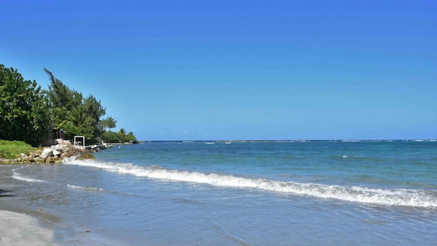 Une plage avec une eau d’un bleu limpide, un rivage sablonneux et quelques zones verdoyantes.