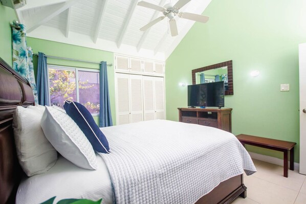 A bedroom with a bed, a ceiling fan, a television on a wooden stand, and a window with curtains. - 3 Bedrm in Richmond Estate Pool Gym Plygrnd Beach (St. Ann's Bay)