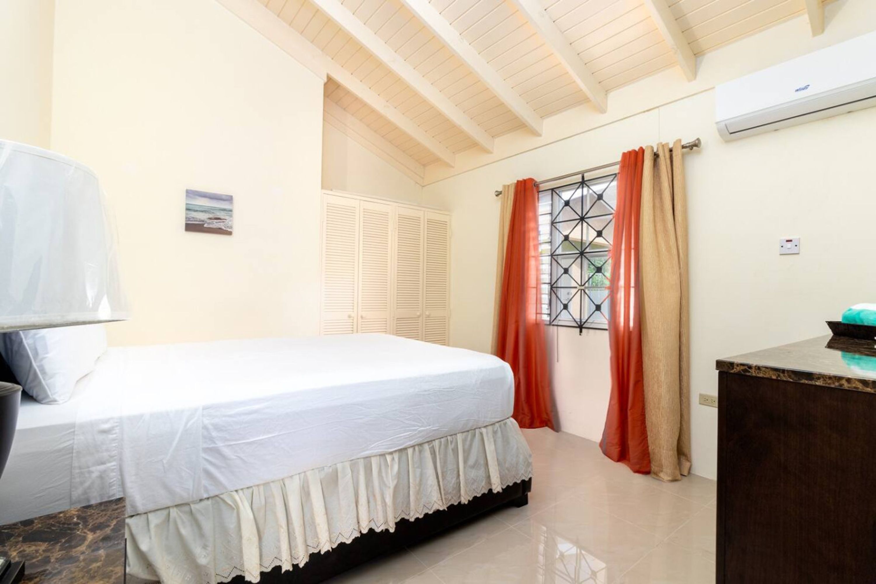 A bedroom with a bed, a desk, a window with curtains, and an air conditioning unit.
