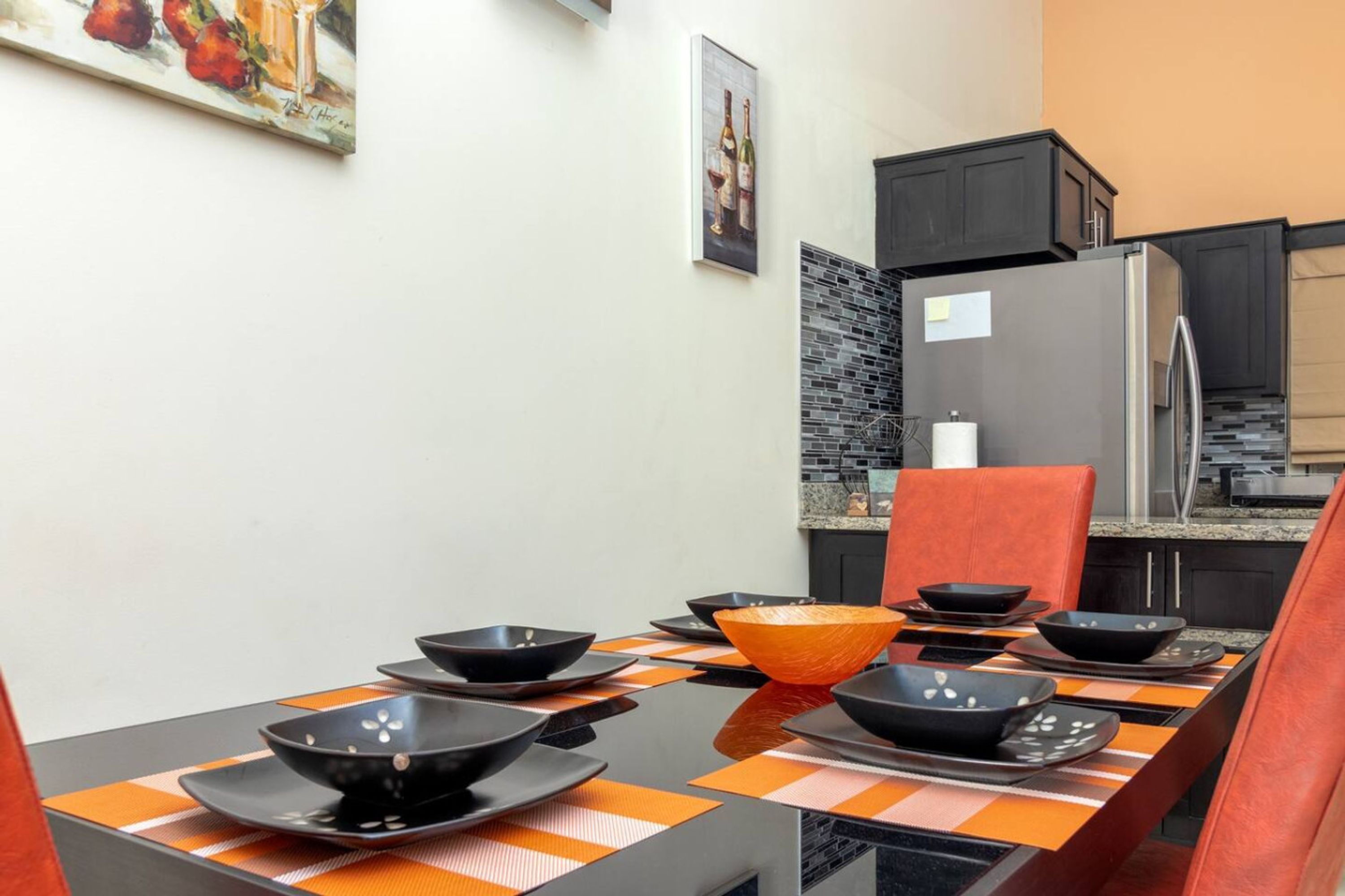 A dining area with a table set for four, black and orange placemats, and a large orange bowl.