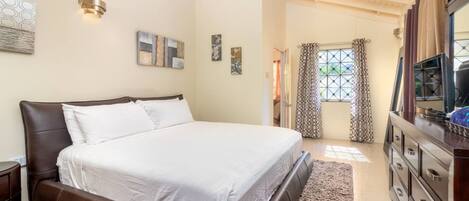 A bedroom with a large bed, a dresser, and a mirror. There are wall art pieces and a window with curtains.