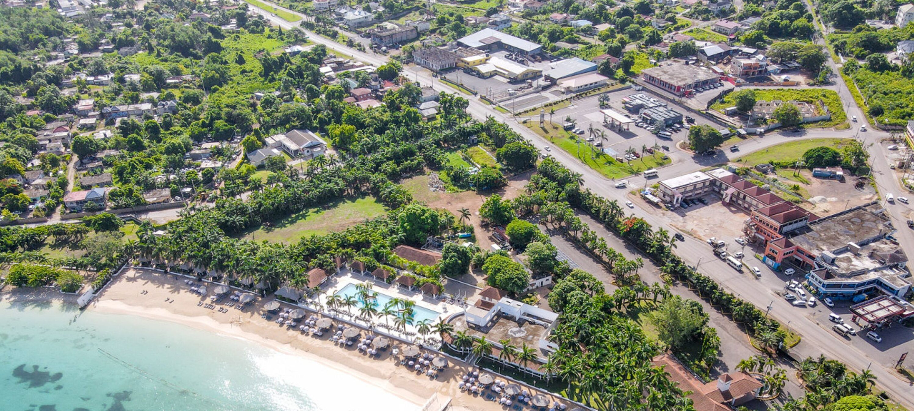Vista aérea de uma cidade costeira com praia, piscina e vários edifícios.