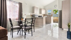 A modern kitchen with a central island, a dining area with a round table and chairs, and a view of the outdoors through a window. - Comfort Arecahomes Beach Access Pool Waterpark (Discovery Bay)