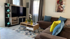 A living room with a flat-screen TV, a brown sofa with colorful cushions, a wooden coffee table, and a patterned rug. - Comfort Arecahomes Beach Access Pool Waterpark (Discovery Bay)