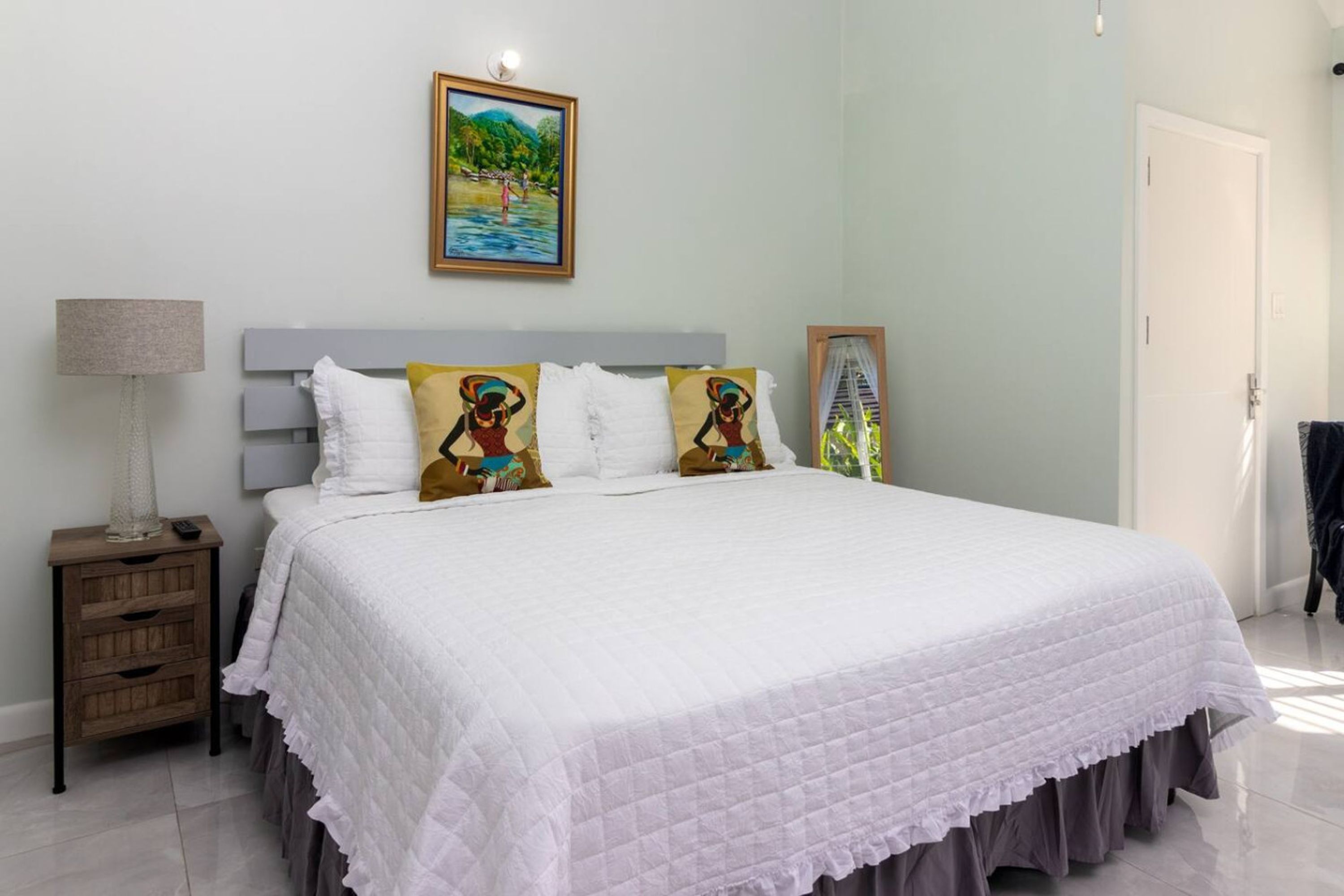 A bedroom with a bed, a nightstand, a lamp, and a painting on the wall.