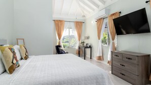 Un dormitorio con cama, cómoda, televisor y ventana con cortinas.