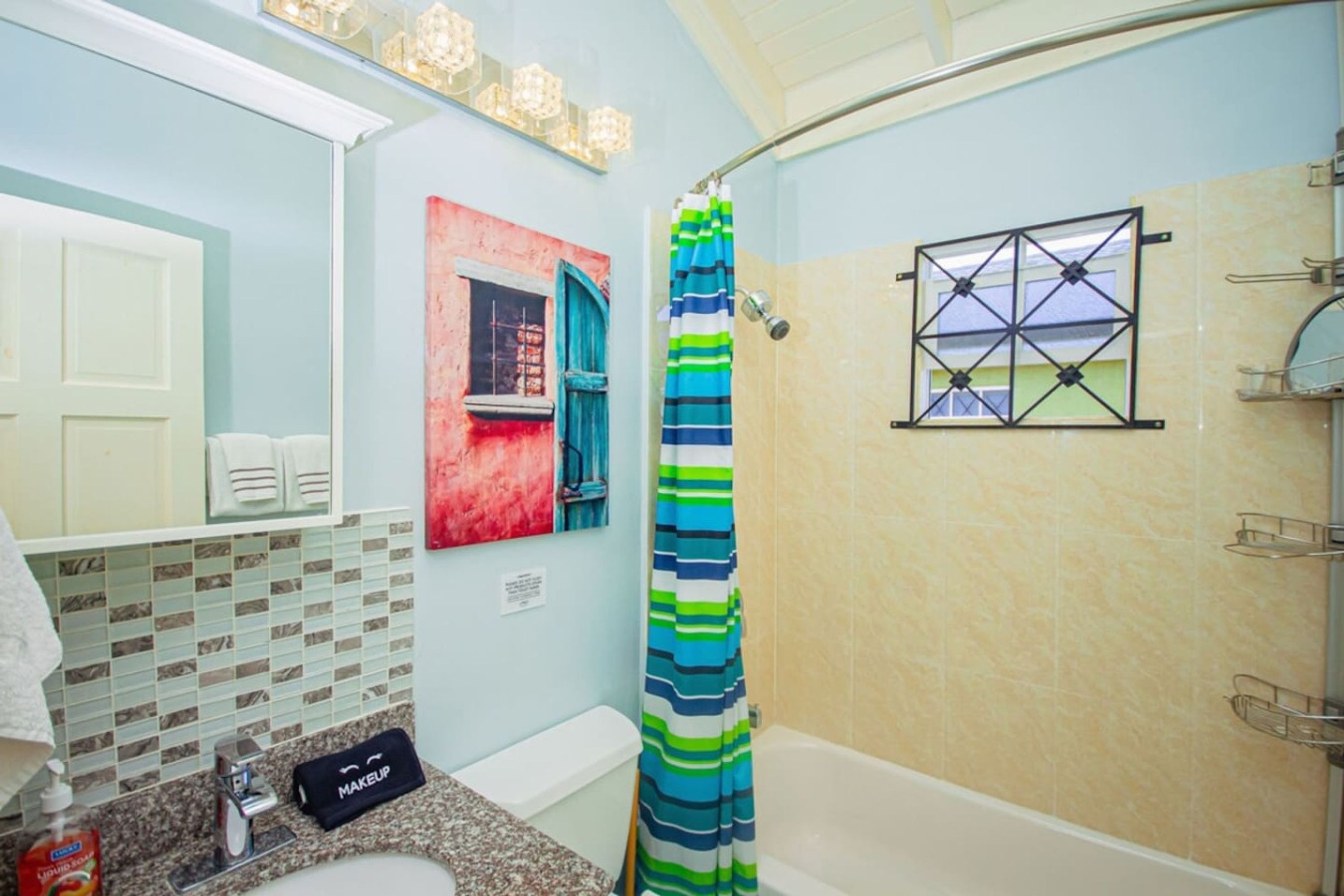 A bathroom with a shower curtain, a bathtub, a sink with a makeup bag, and a towel rack.