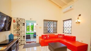 A living room with a red sofa, a grey ottoman, and a TV on the wall. - Adorable Beach House in Drax Hall Gated Pool Gym (St. Ann's Bay)