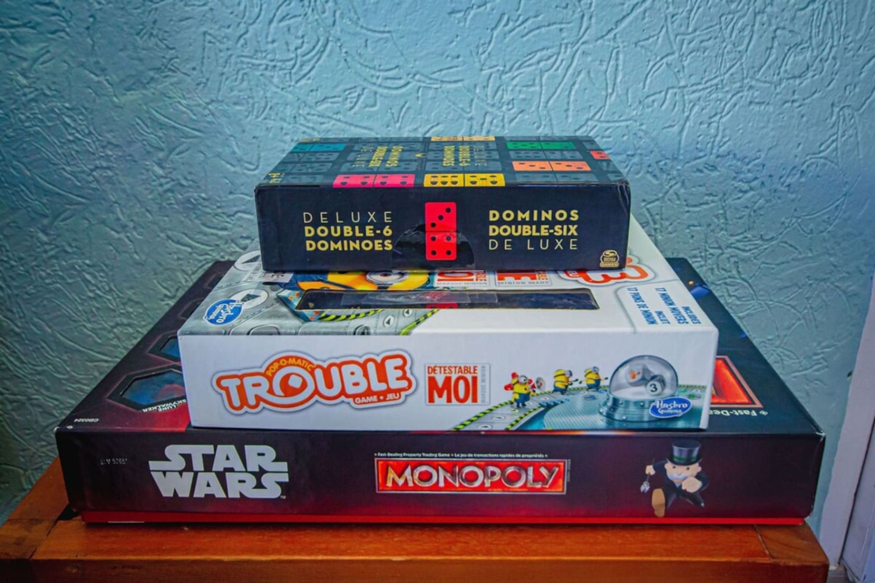 A stack of board games including Star Wars, Monopoly, and others on a wooden surface.