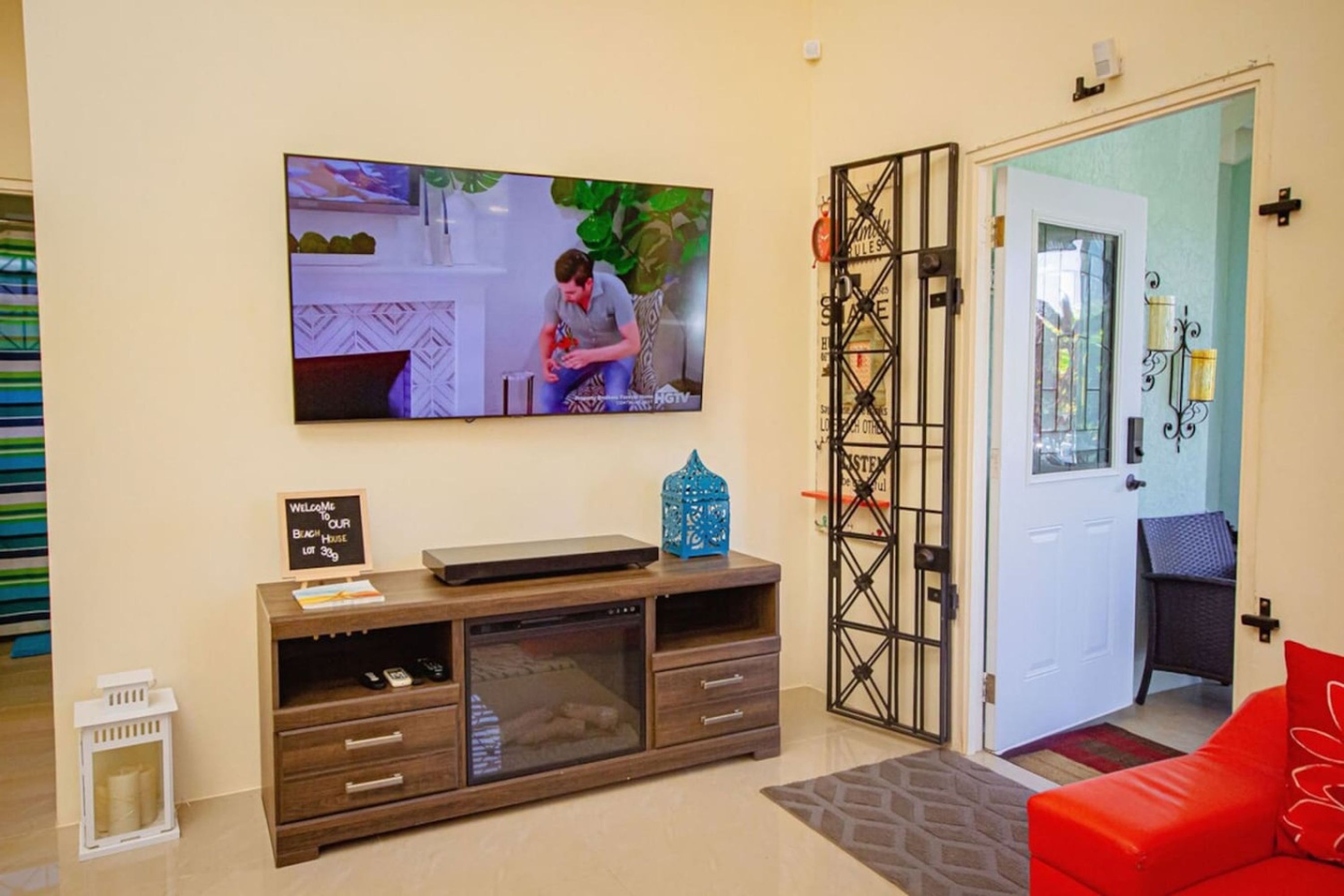 A living room with a television, a wooden entertainment unit, a red sofa, and a door with decorative ironwork.