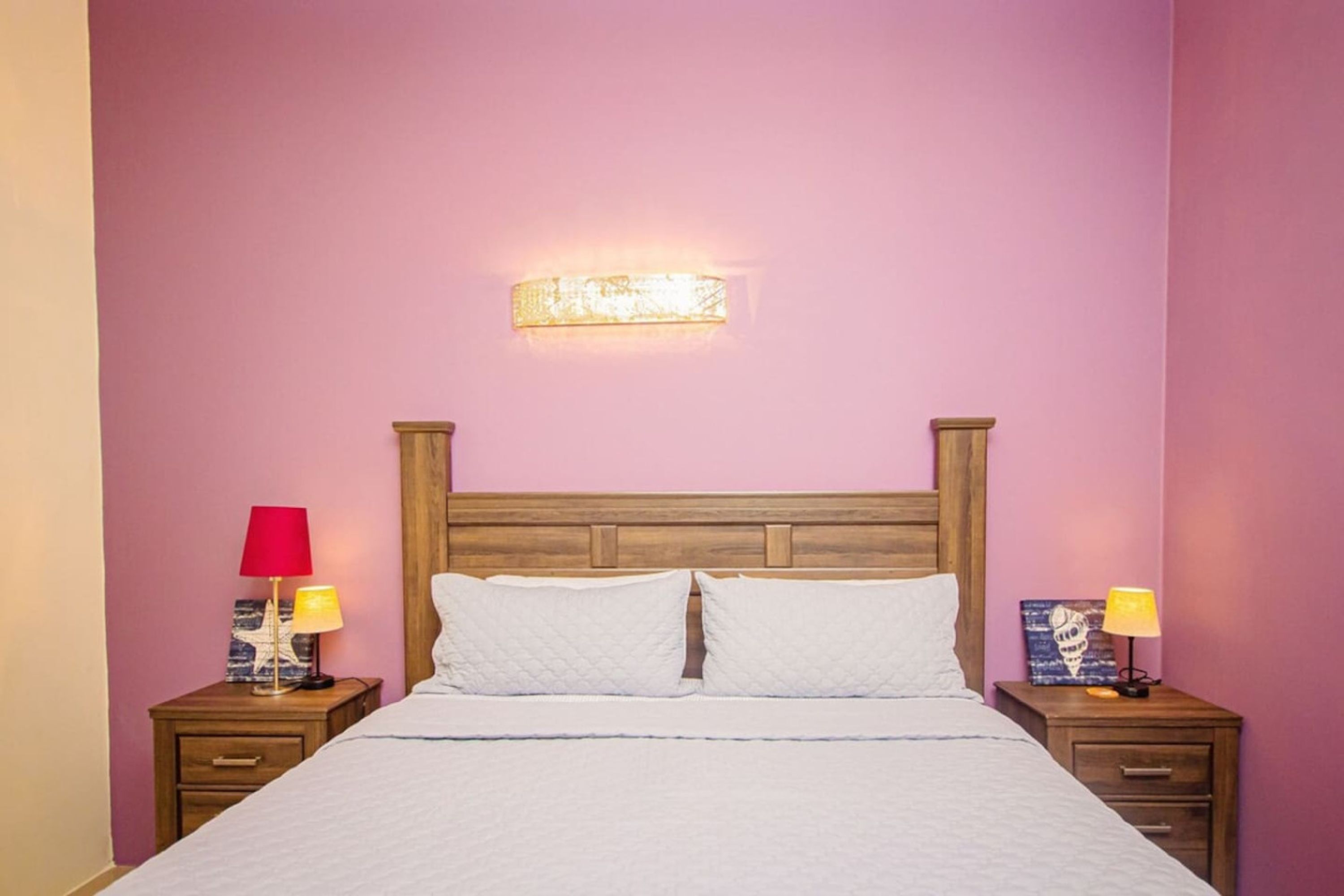 A bedroom with a wooden headboard, a bed with white bedding, two bedside tables with lamps, and a wall-mounted light fixture.