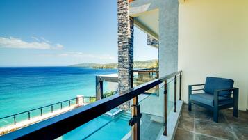 A balcony with a glass railing overlooking a pool and the ocean.