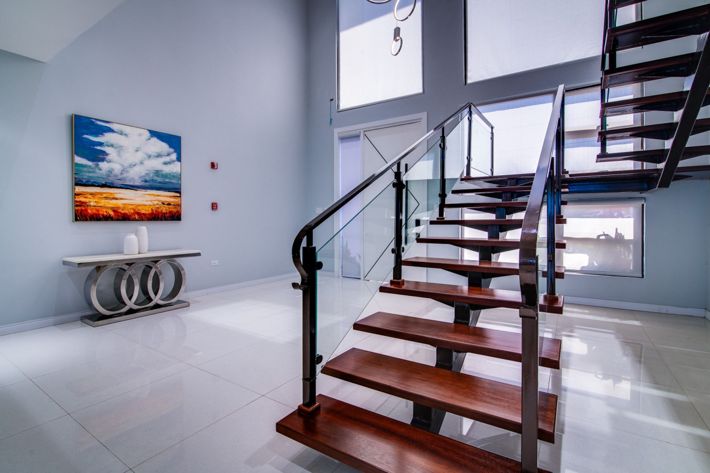 A modern interior with a wooden staircase, a painting of a sunset, and a minimalist console table.