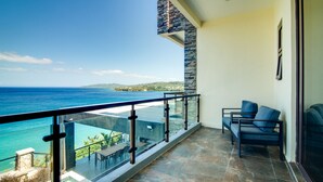 A balcony with a view of the ocean and a stone wall. There are two chairs and a table on the balcony. - Luxury Oceanfront Villa Fully Staffed Pool Jacuzzi Movie Theatre (Tower Isle)