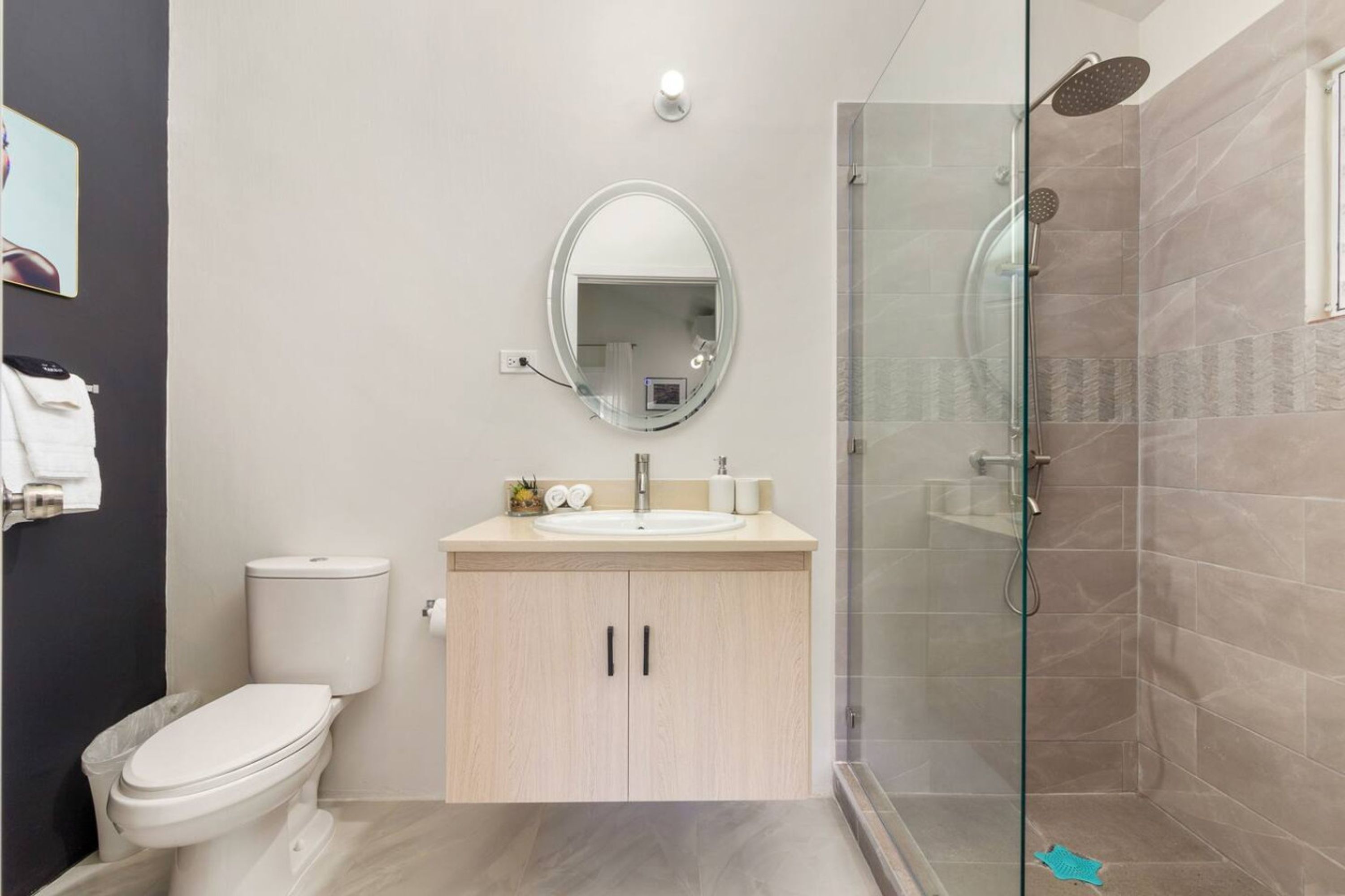 Et moderne badeværelse med toilet, vask og glasvæg omkring brusebad.