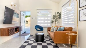 Una sala de estar moderna con un tapete a cuadros, un sofá marrón, un sillón azul, una mesita redonda y un televisor montado en la pared.