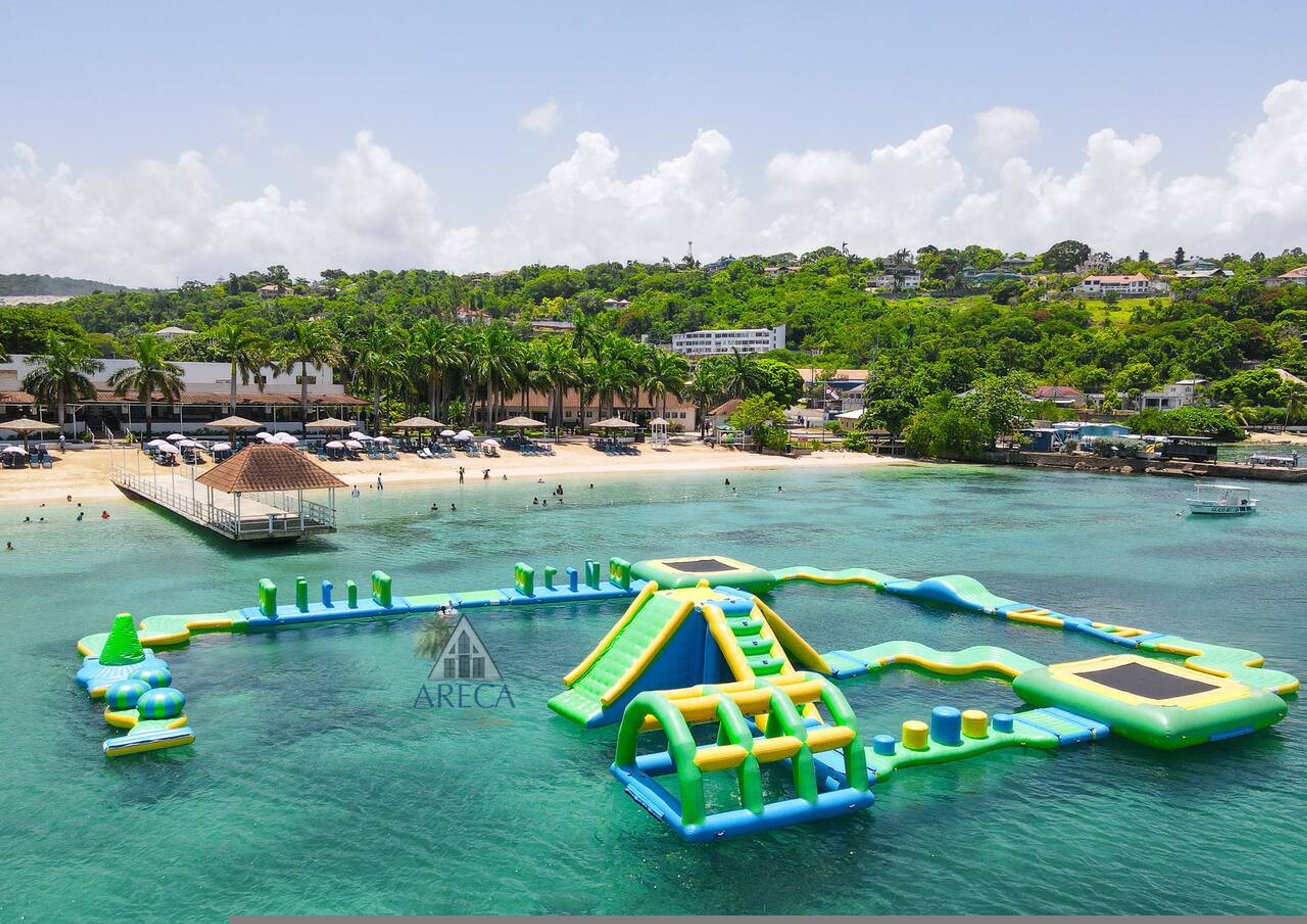 A beach resort with a water park, including inflatable play structures and a beach area with umbrellas and lounge chairs.