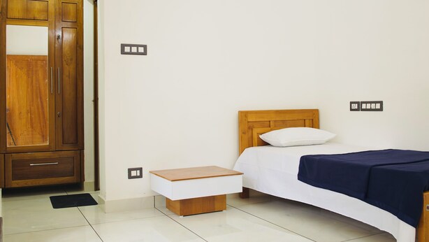 Ein Schlafzimmer mit einem Holfischschrank, einem Nachttisch, einem Bett mit weißer und dunkelblauer Bettdecke sowie einem Holz-Kopfteil.