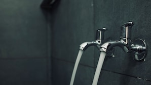 Ein Badezimmer mit zwei chromfarbenen Wasserhähnen an einer dunkel gefliesten Wand.