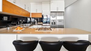 A modern kitchen with a central island, stainless steel appliances, and black bar stools.