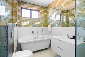 Un baño moderno con salpicadero de azulejos hexagonales, una bañera independiente, un lavabo blanco y un box de ducha de vidrio.