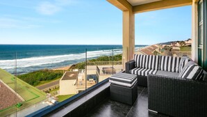 A balcony with a view of the ocean, wicker furniture, and a clear sky.