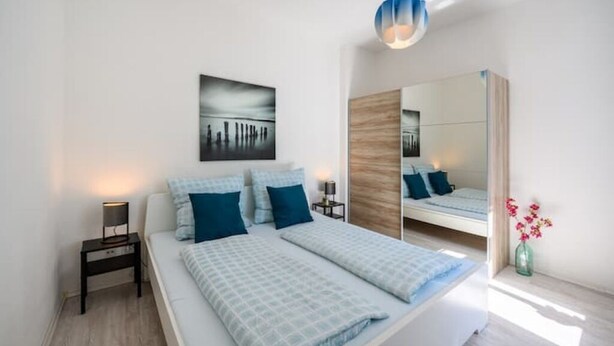 A modern bedroom with a bed, bedside tables, a mirror, and a wall-mounted artwork.