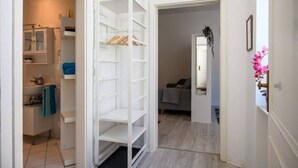 A hallway leading to a bathroom with a white vanity and shelves.