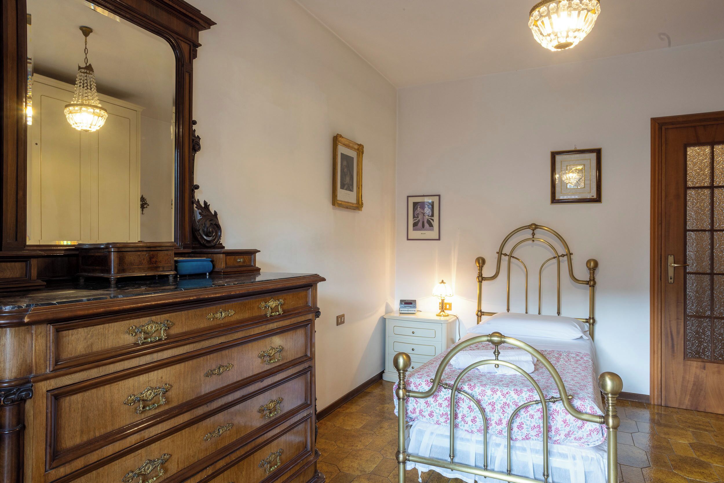 Une chambre à coucher avec une commode en bois, un lit avec un cadre en métal, une table de chevet et un lustre.