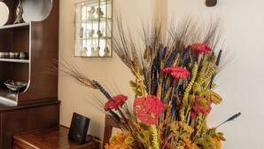 Et værelse med et træskrivebord, en stol, en dekorativ vase med blomster, et vægur og et spejl.