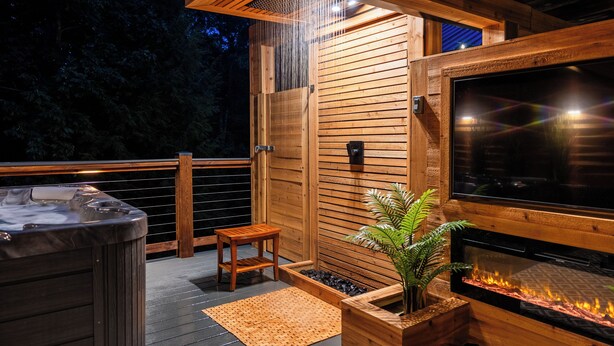 Une terrasse en bois avec un jacuzzi, une petite table en bois, un foyer et un sauna en bois.