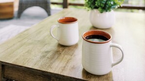 Une table en bois avec deux tasses blanches et une petite plante en pot.