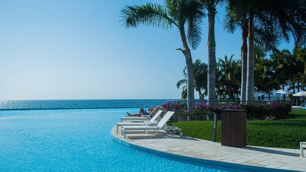 A poolside area with lounge chairs, palm trees, and a view of the ocean. - Beachfront Peninsula PV 8th Floor (Puerto Vallarta)