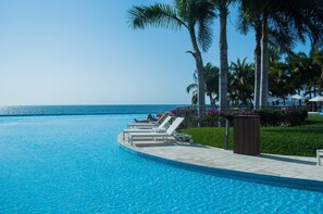 A poolside area with lounge chairs, palm trees, and a view of the ocean.