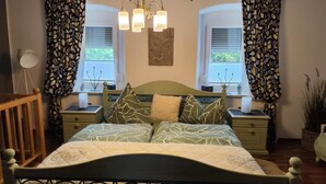 Une chambre à coucher avec un lit, deux tables de chevet, une commode, un lustre et des rideaux.
