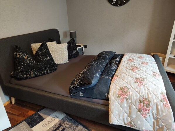 Una cama con cubrecolcha acolchado, varios almohadones y una mesita de noche con lámpara.