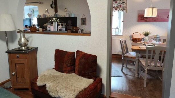 Un salon chaleureux avec un canapé, une lampe et une vue sur la cuisine grâce à une arche.