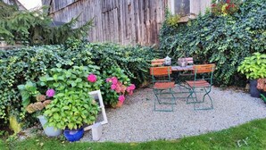 Une terrasse de jardin avec une table et des chaises en bois, entourée de plantes en pot et d’une clôture en bois.