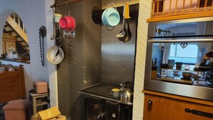 Une cuisine avec un poêle, des casseroles suspendues et un panier de bois de chauffage.