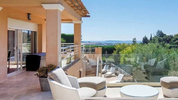 A balcony with outdoor furniture, a glass railing, and a view of greenery and distant buildings. - Villa on the hills of Mandelieu with sea view and swimming pool (Mandelieu-la-Napoule)