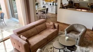 A living room with a sofa, armchair, and coffee table, a kitchen in the background, and a sliding glass door leading to an outdoor area. - Villa on the hills of Mandelieu with sea view and swimming pool (Mandelieu-la-Napoule)