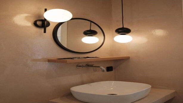Une salle de bain moderne avec un lavabo blanc, un miroir rond et deux lampes suspendues.
