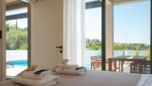 Une chambre d’hôtel avec un lit, une vue sur la piscine et un balcon aménagé avec du mobilier d’extérieur.