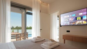 A hotel room with a bed, a TV mounted on the wall, and a balcony with a table and chairs. - VILA1 ANAPNOE IKIES CORFU WITH PRIVATE POOL (Corfu)