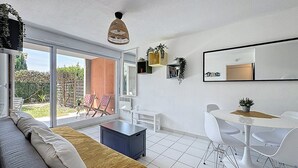 Un salon moderne comprenant un canapé, une table à manger avec des chaises, un luminaire suspendu et une porte-fenêtre coulissante donnant sur un patio.